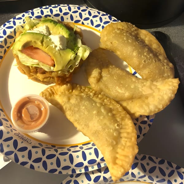 A Mexican tostada with avocado, lettuce, and tomato, alongside three golden-fried empanadas and sauce.