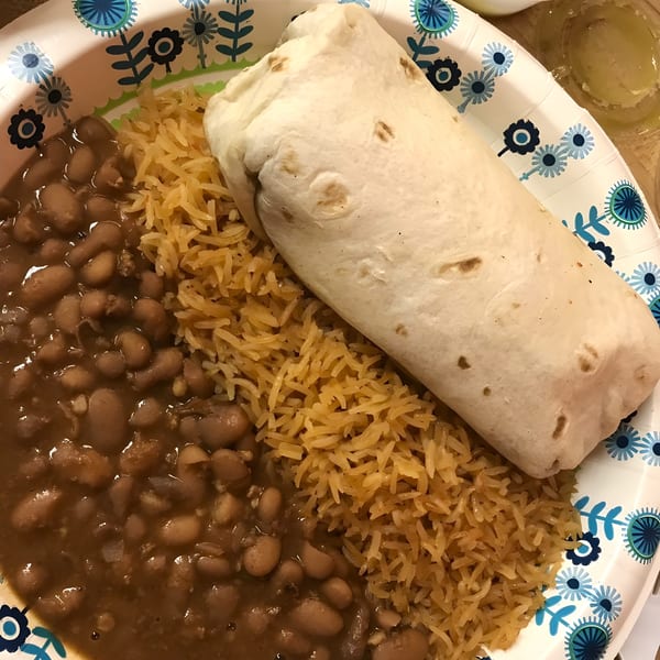 A burrito, rice, and beans on a floral paper plate from Taqueria y Pupuseria To Go.